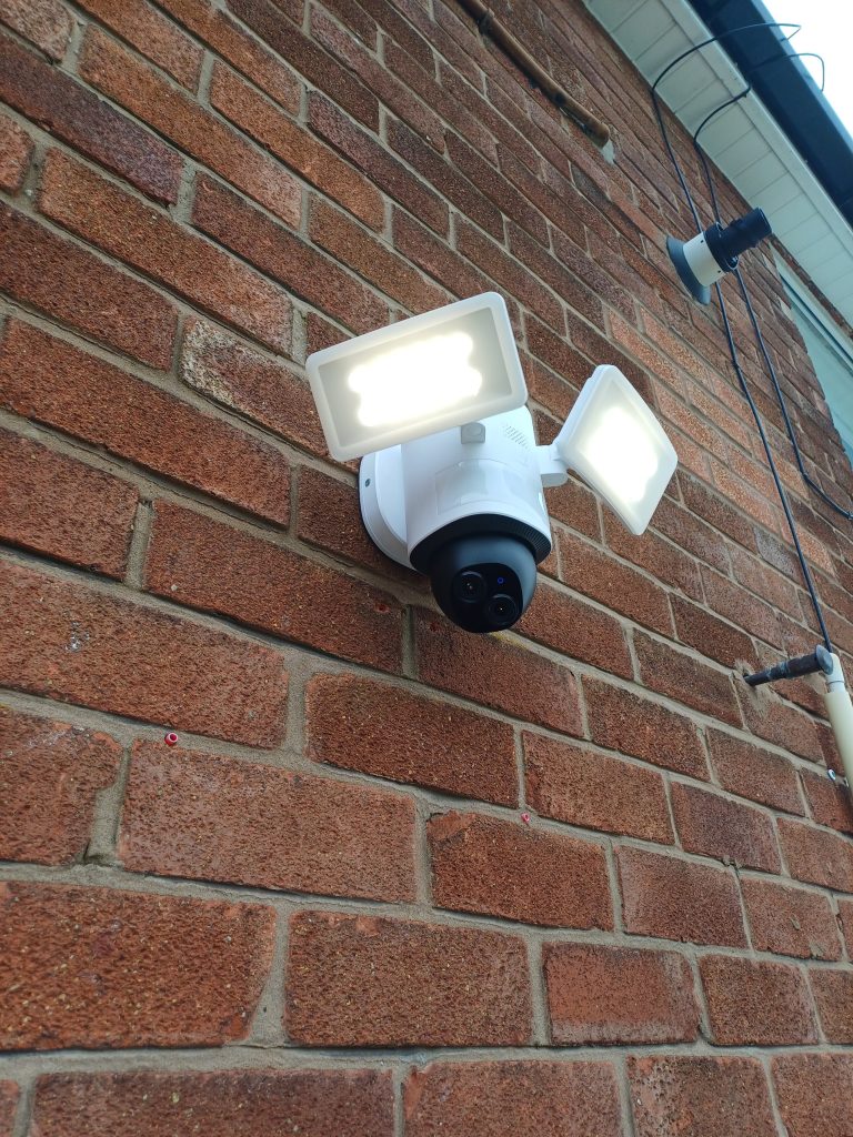 Twin LED floodlight with a built-in security camera on a brick wall