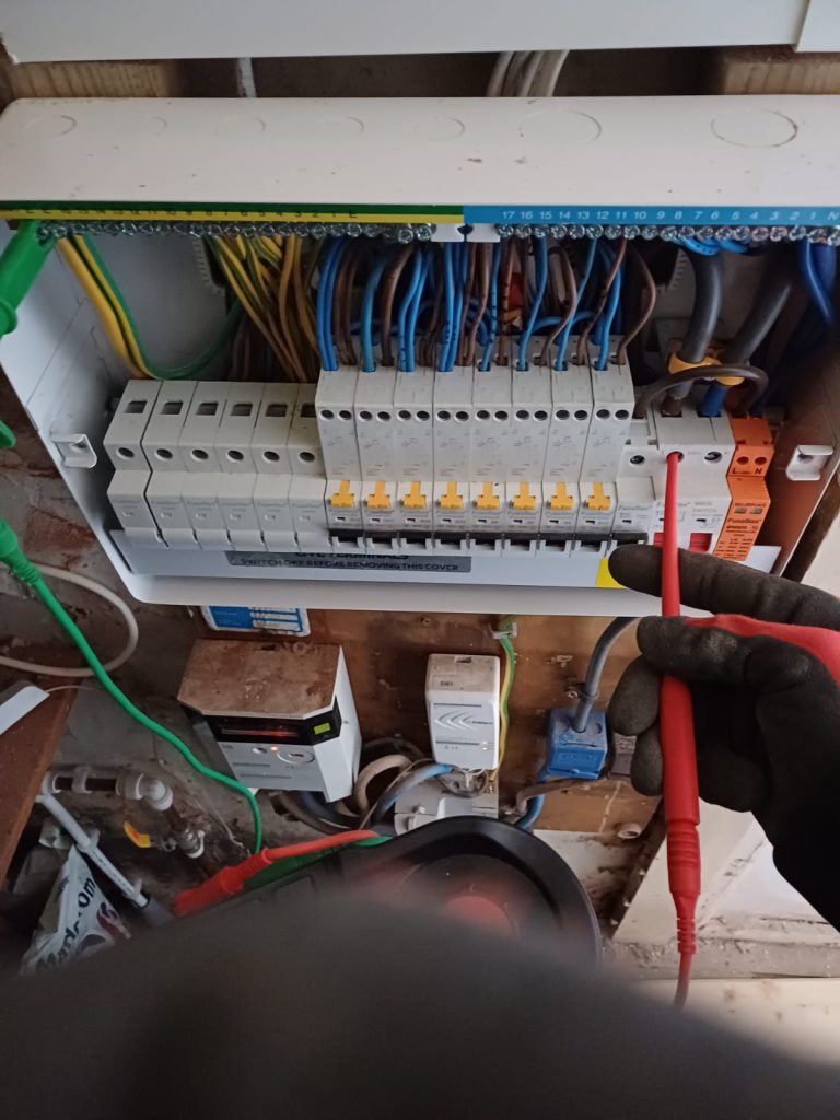Electrician holding test probes against a consumer unit while tracing a fault